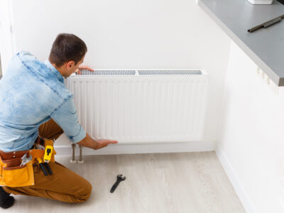 Man is repairing radiator battery in the room. Maintenance repair works renovation in the flat. Heating restoration. Wrench in hands.