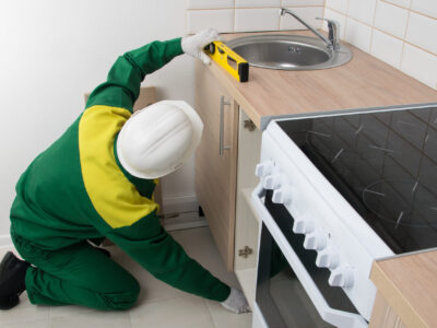 a specialist checks the evenness of the installation of kitchen furniture with a tool, turns the cabinet legs to adjust the level, side view